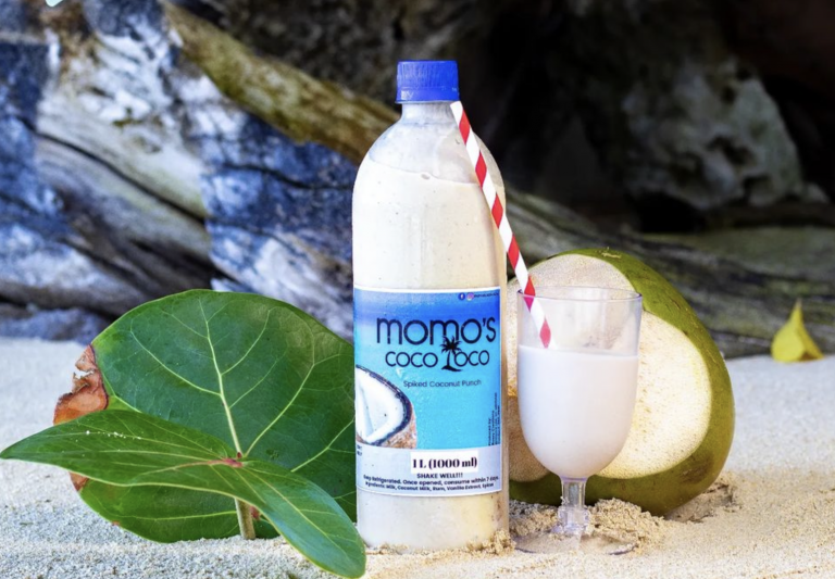 A bottle of Momo's Coco Loco drink with a glass and straw and a coconut